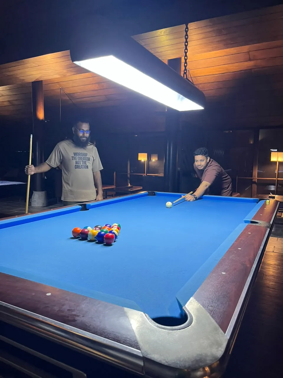 Two teammates at the pool table under a hanging light
