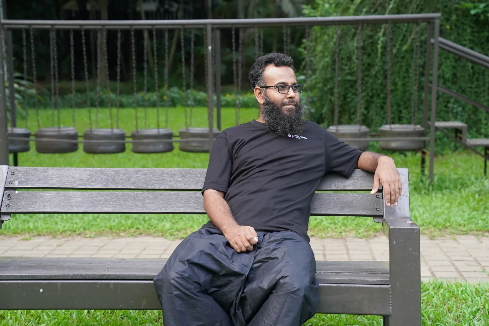 Reclining on a park bench with tire swings on the lawn behind