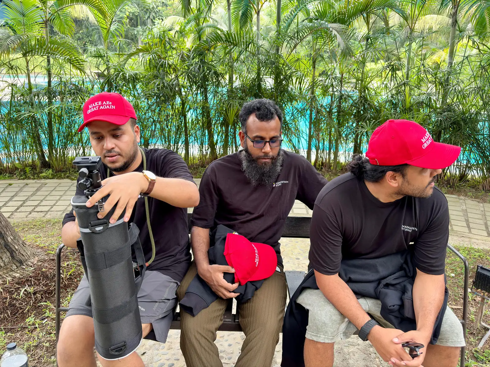 Teammates on a bench by the pool in matching red caps, setting up a tripod