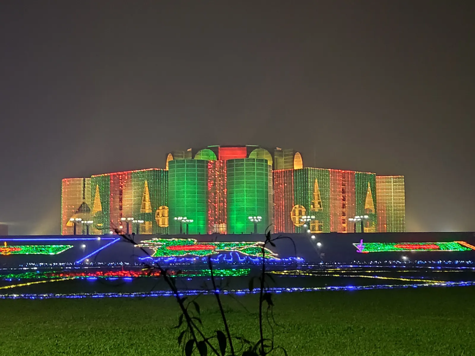 The National Parliament building floodlit in green and red at night, Dhaka