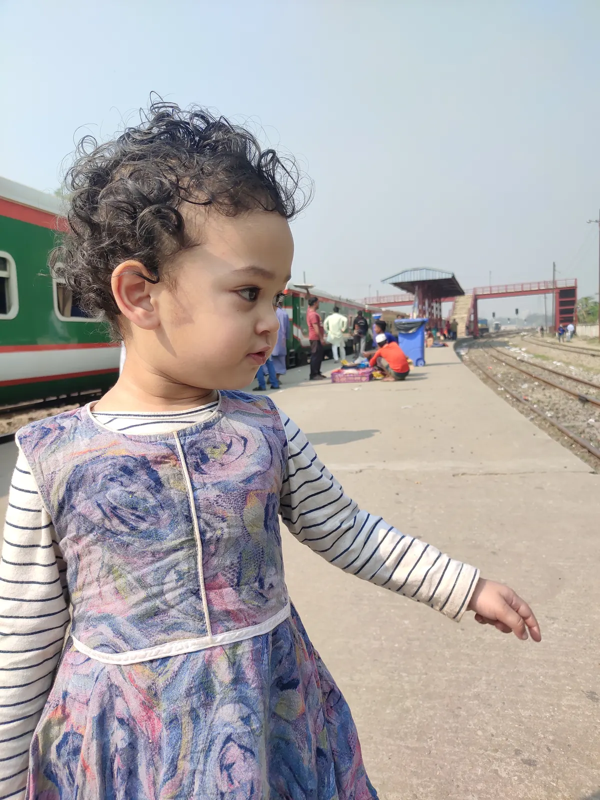 A toddler in a floral dress on the railway platform, train waiting behind