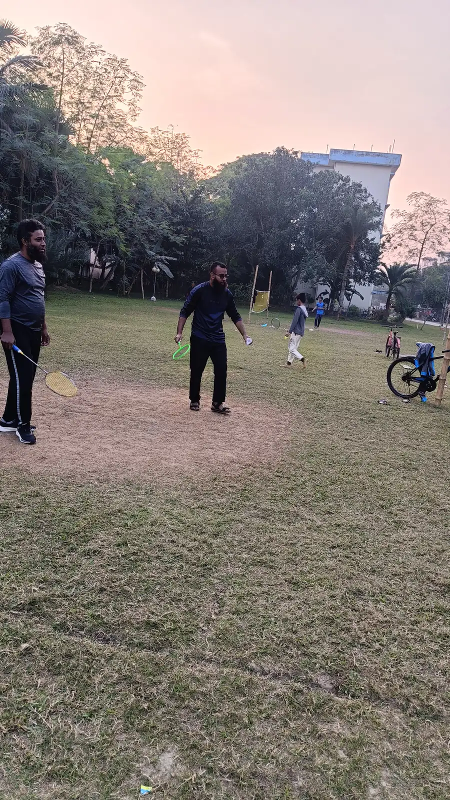 Badminton on the field at dusk, rackets mid-swing