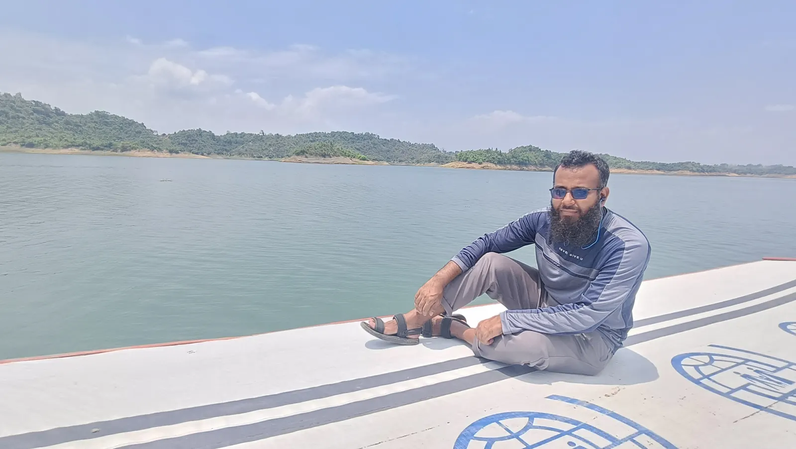 Sitting on the roof of the boat as it crosses Kaptai Lake, hills behind
