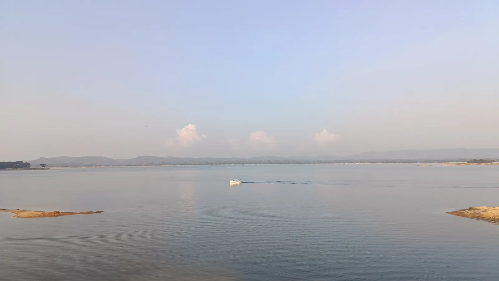 A single boat crossing the wide, still lake under a pale sky
