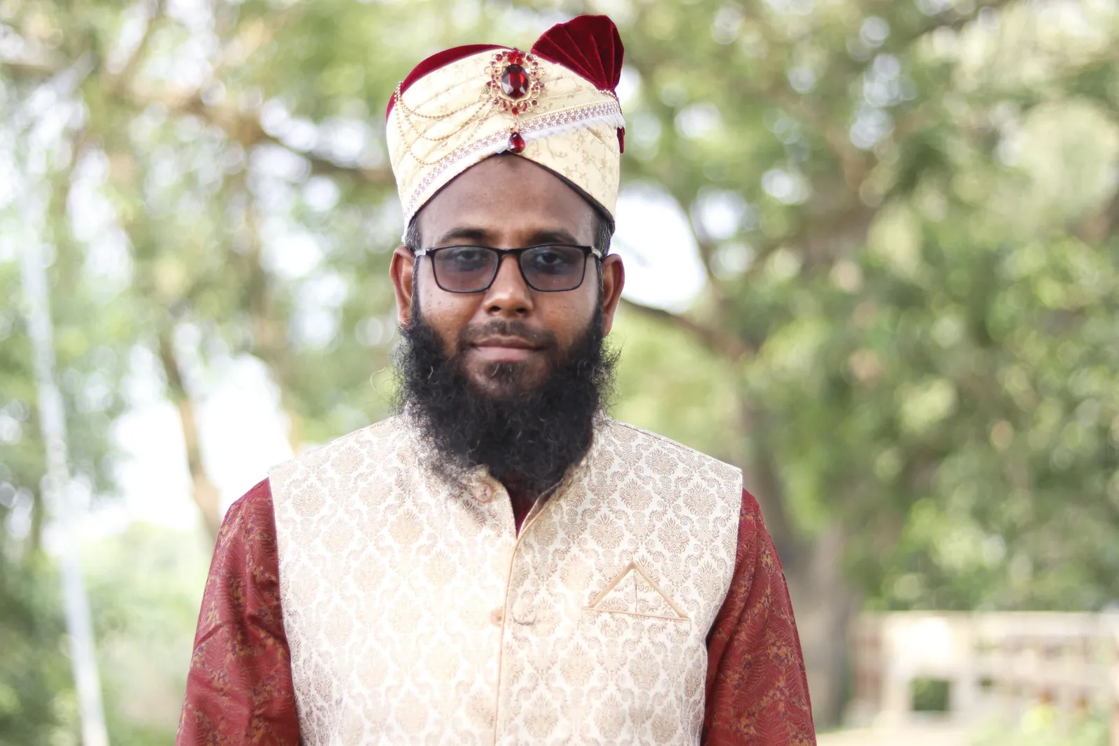 Groom portrait in a jeweled cream-and-maroon wedding turban and brocade vest