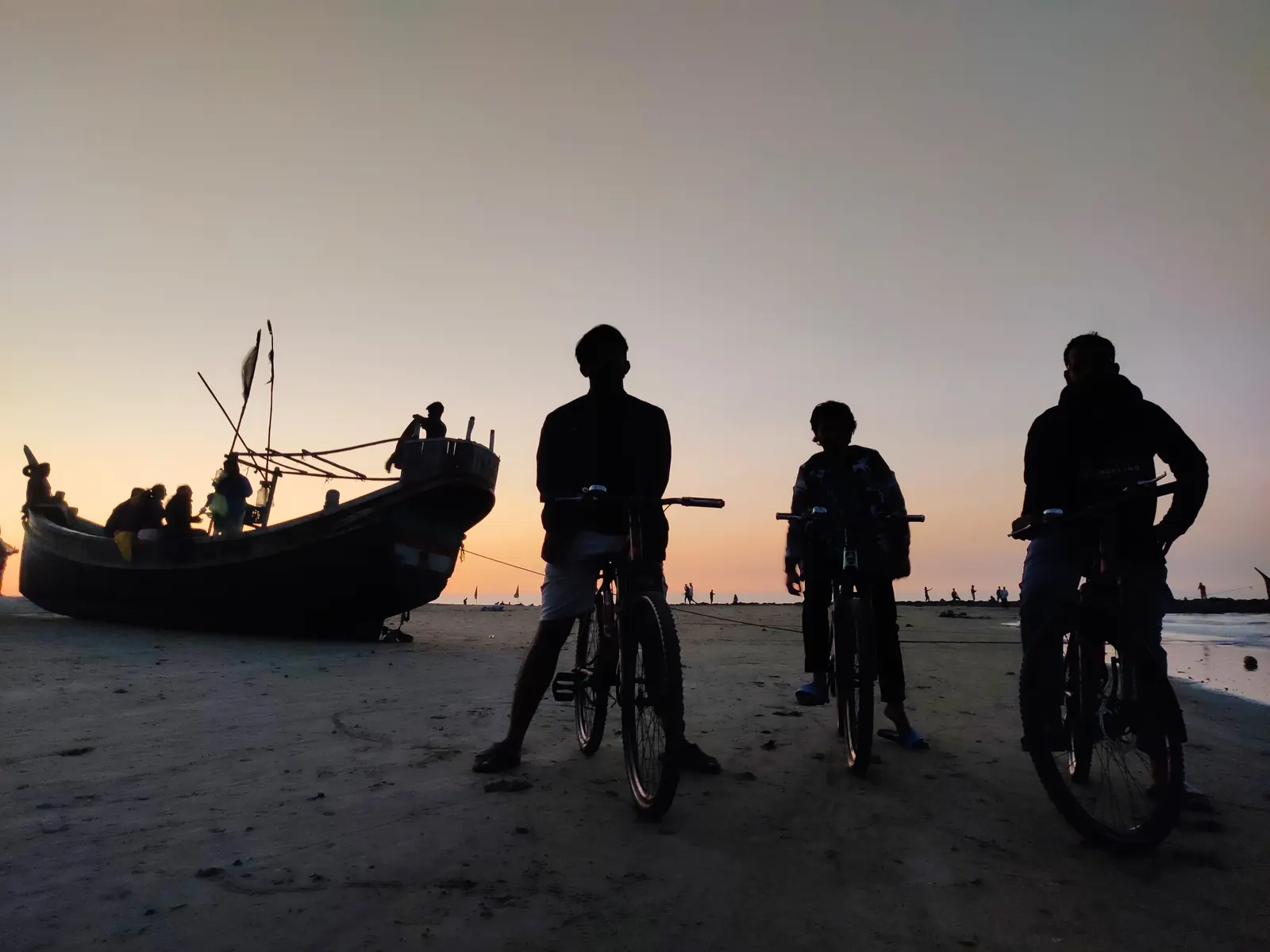 Cyclists silhouetted beside a fishing boat as the sun drops behind them