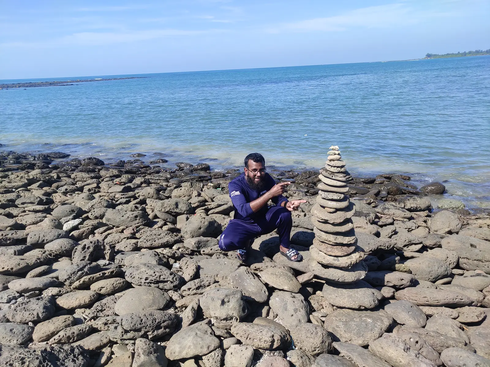 Crouched beside a stacked stone cairn on the coral shore, sea behind