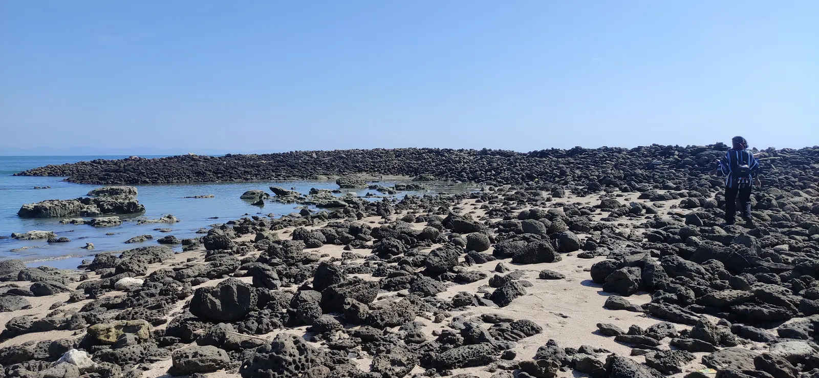 A lone figure out on the coral shelf, water flat to the horizon