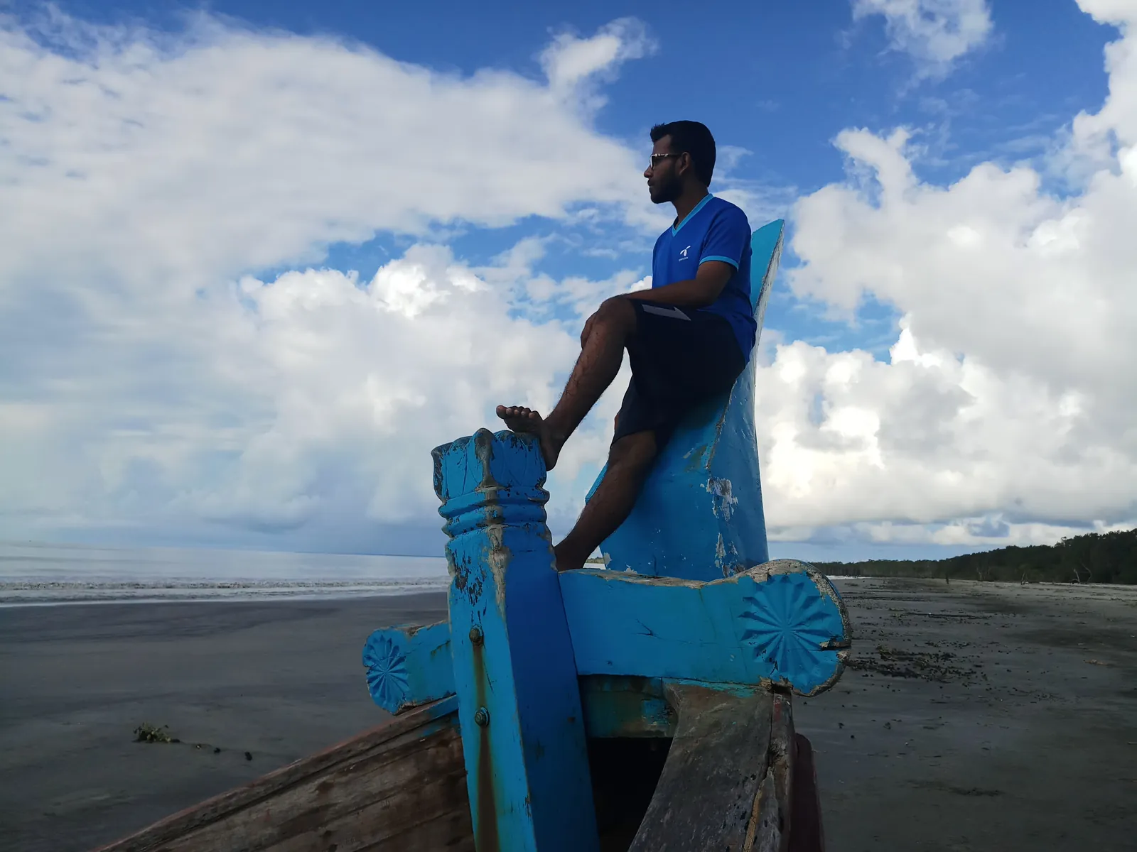 Sitting on the carved blue bow of a beached fishing boat under big clouds