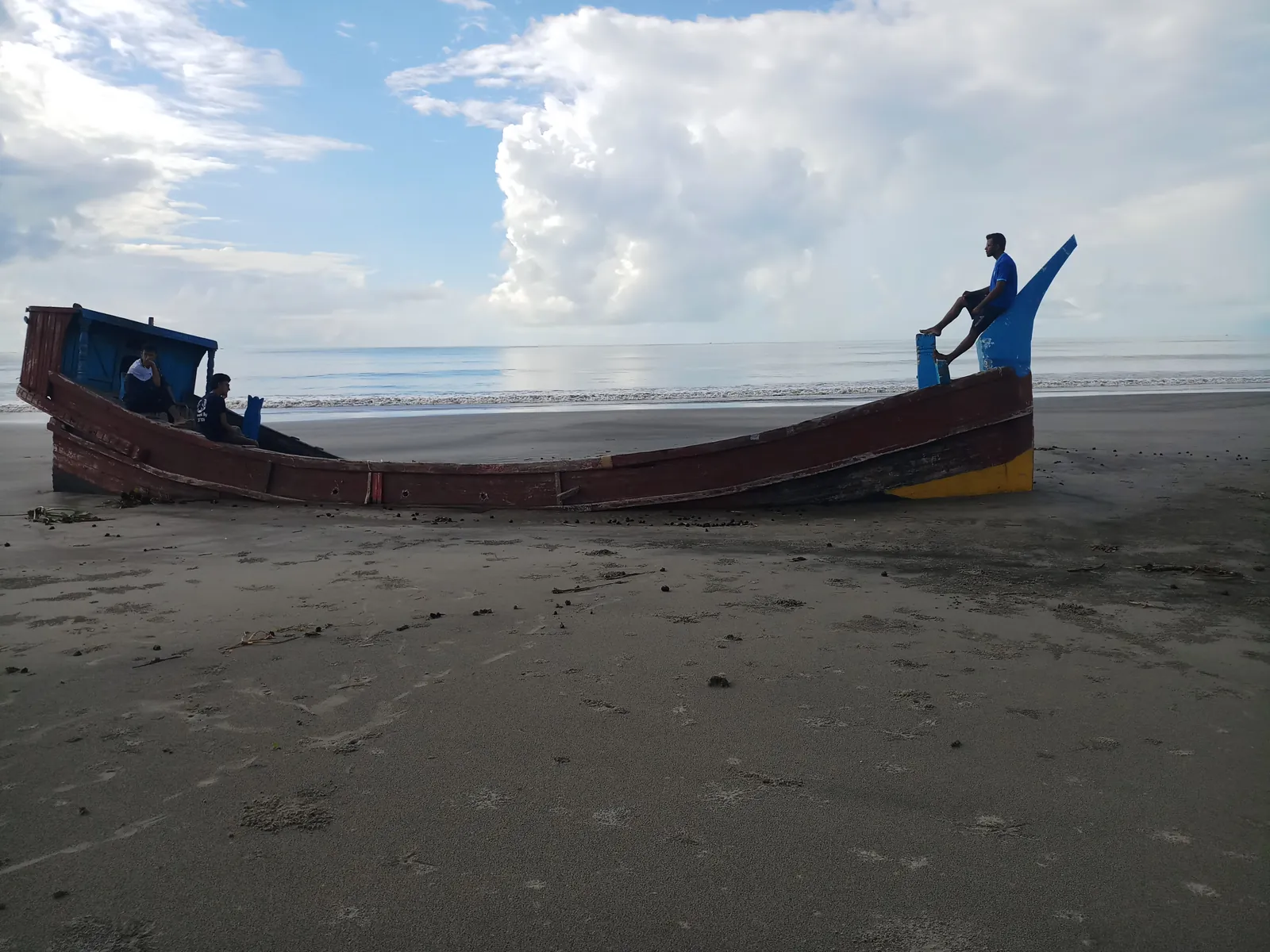 A long wooden boat beached on the wet tidal sand